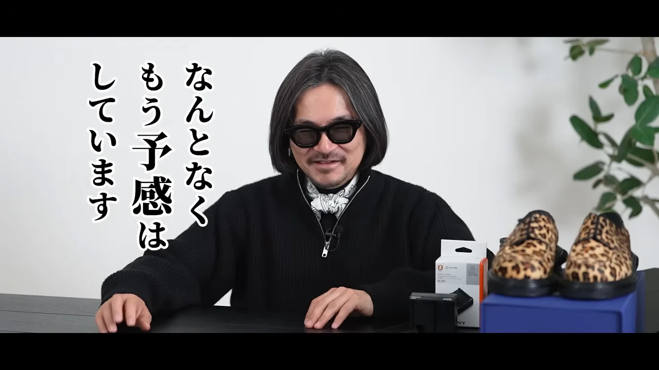 机の前に座って話しているサングラスをかけた男性