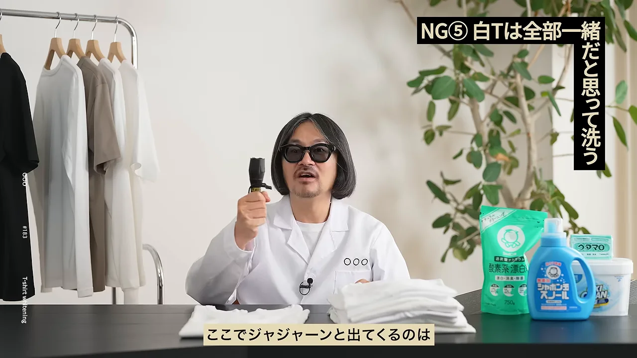 白衣姿の男性が机の前で小型のブラックライトを手に持ち、前を向いて説明している様子。