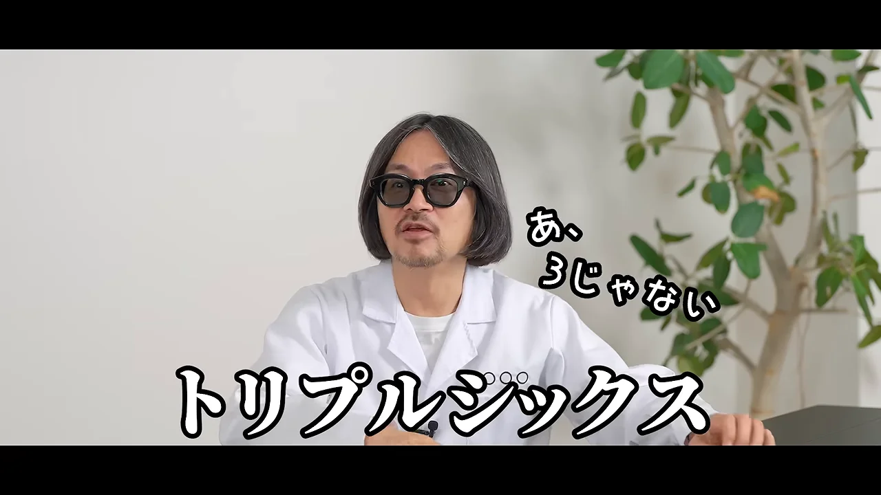 白衣を着た男性が観葉植物を背景にして正面を見つめながら話している様子。