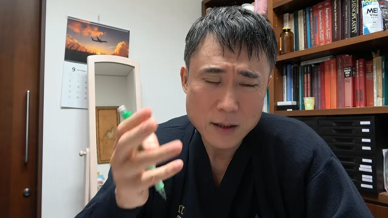 本棚の前に座る男性が手にペンを持って正面を見つめながら話している様子