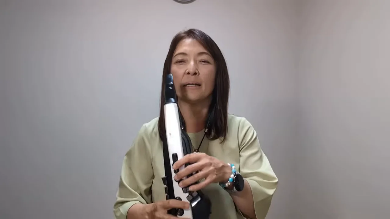 電子管楽器を両手で持ちながらカメラに向かって語る女性の姿。