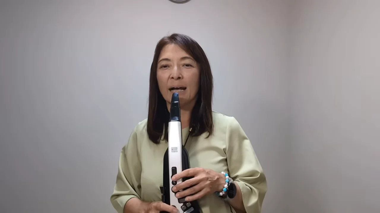 電子管楽器を構えながら正面を向いて話す女性の姿。