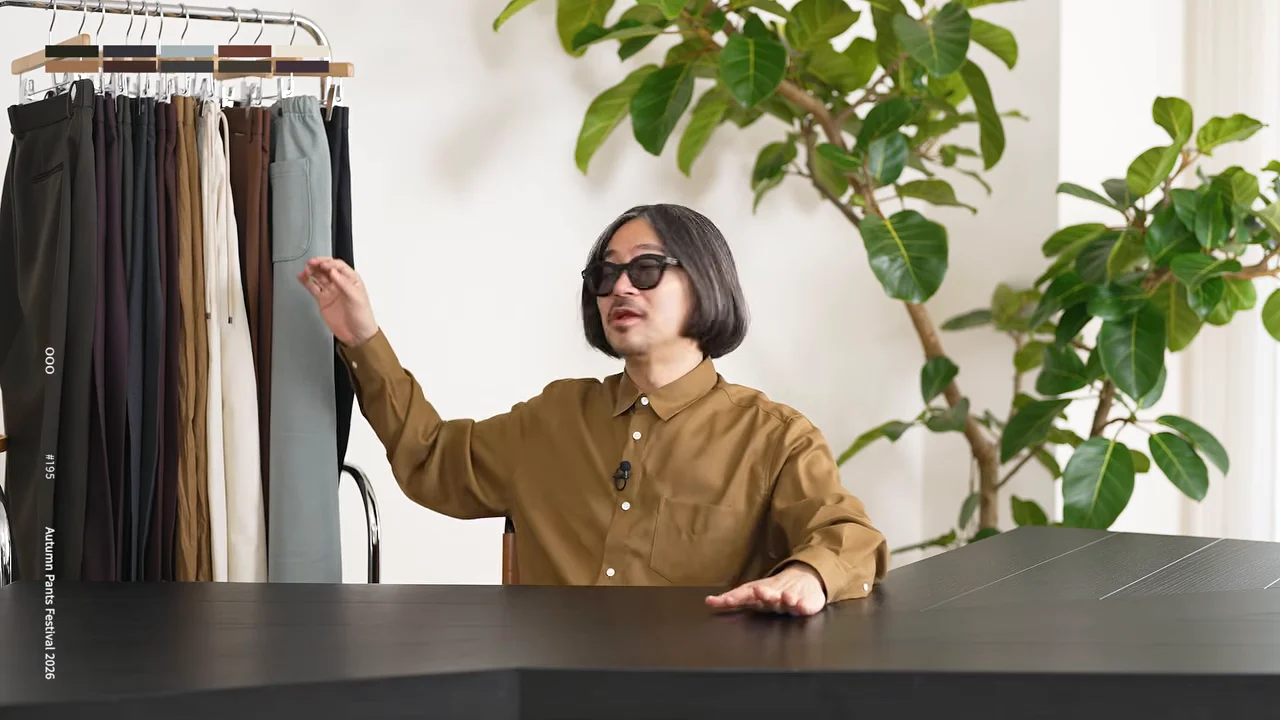 男性が洋服ラックに掛けられたパンツを指差しながら話している。