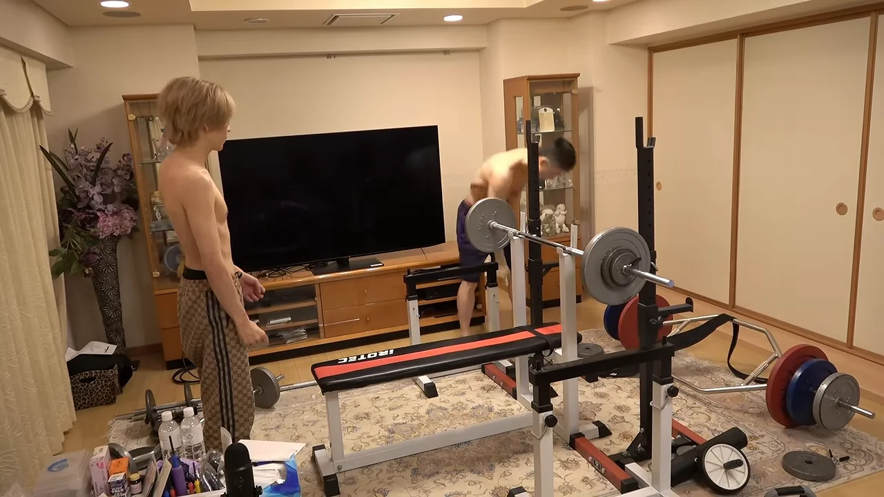 上半身裸になった2人の男性が、ベンチプレスの器具の前で準備をしています。