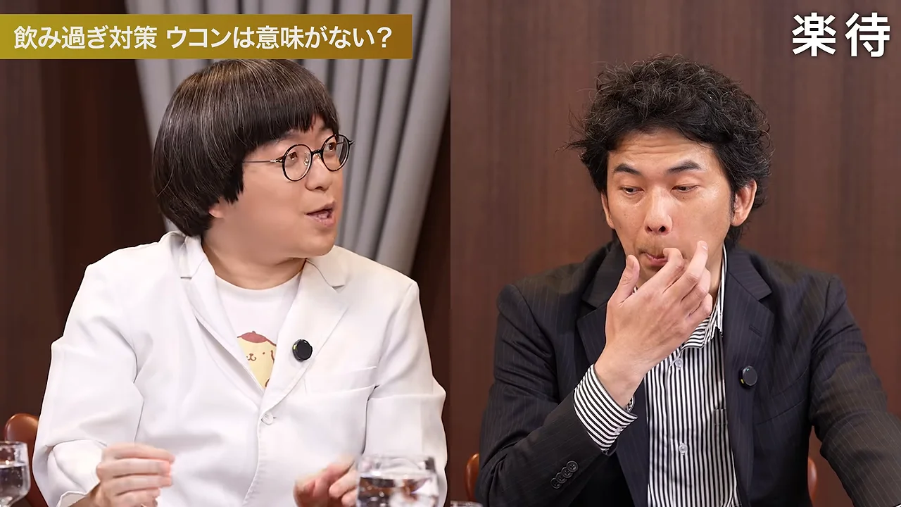 白衣の男性が話す横で、スーツの男性が口元に指を当てて聞いています。