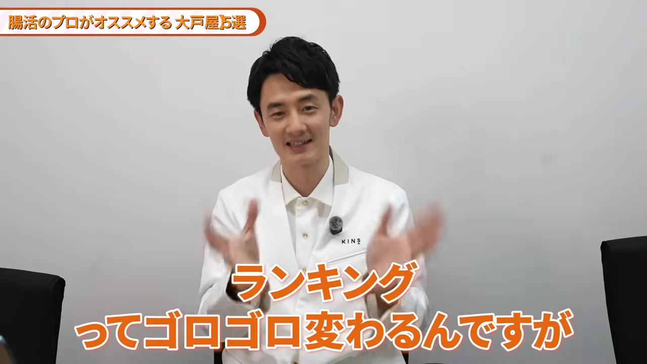 白衣を着た男性が手を動かしながら話している様子