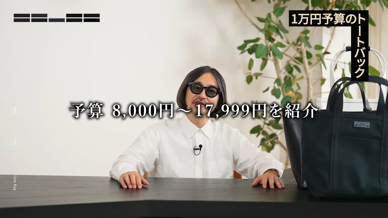 白いシャツを着てサングラスをかけた男性が机の前に座り、横に置かれたトートバッグを紹介しています。