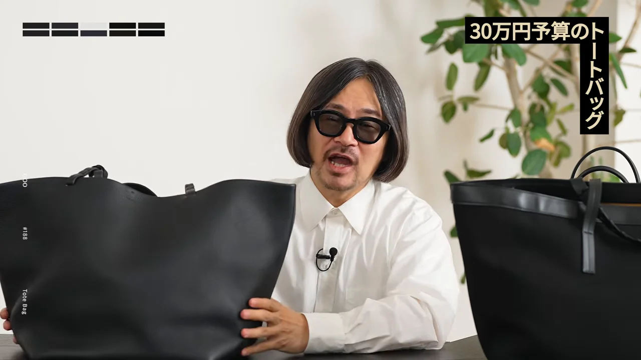 サングラスをかけた男性が机の上で大きな黒いトートバッグを両手で持っています。