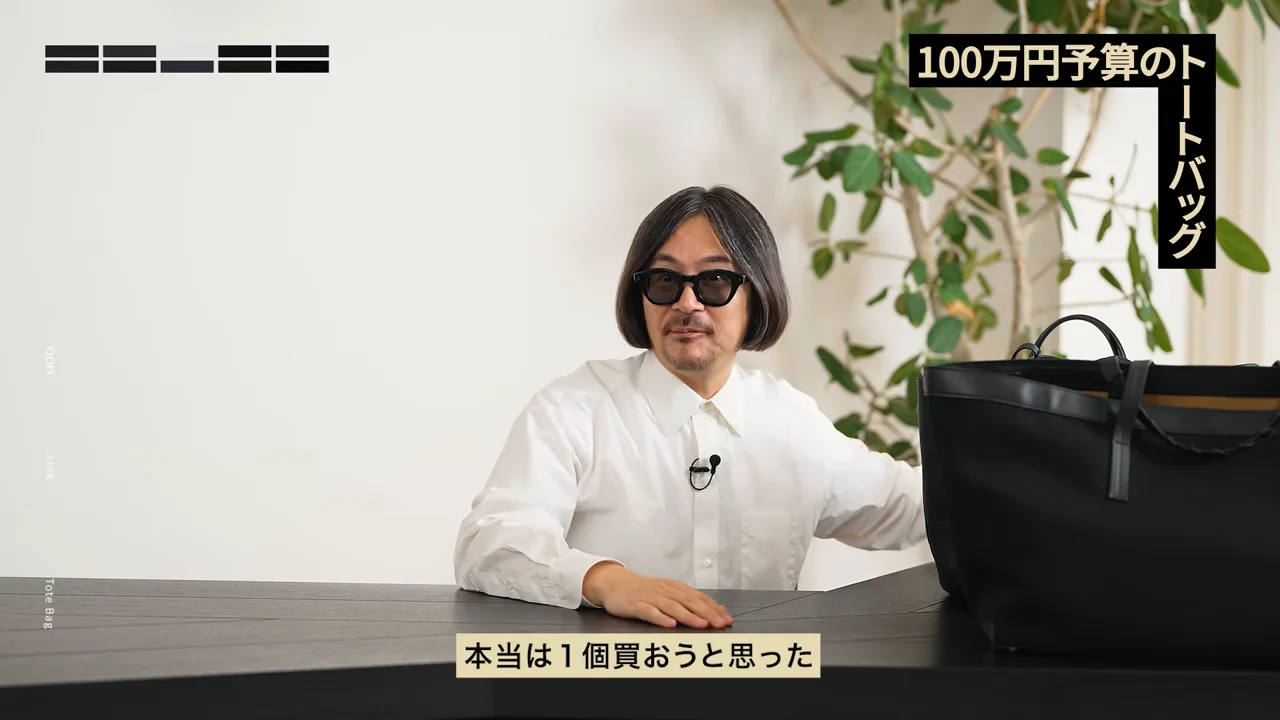 男性が机に両手を置き、横に置かれた大きな黒いバッグの横で話しています。