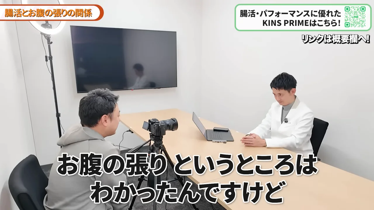 机の上にカメラとノートパソコンが置かれ、二人の男性が向かい合って座っています。