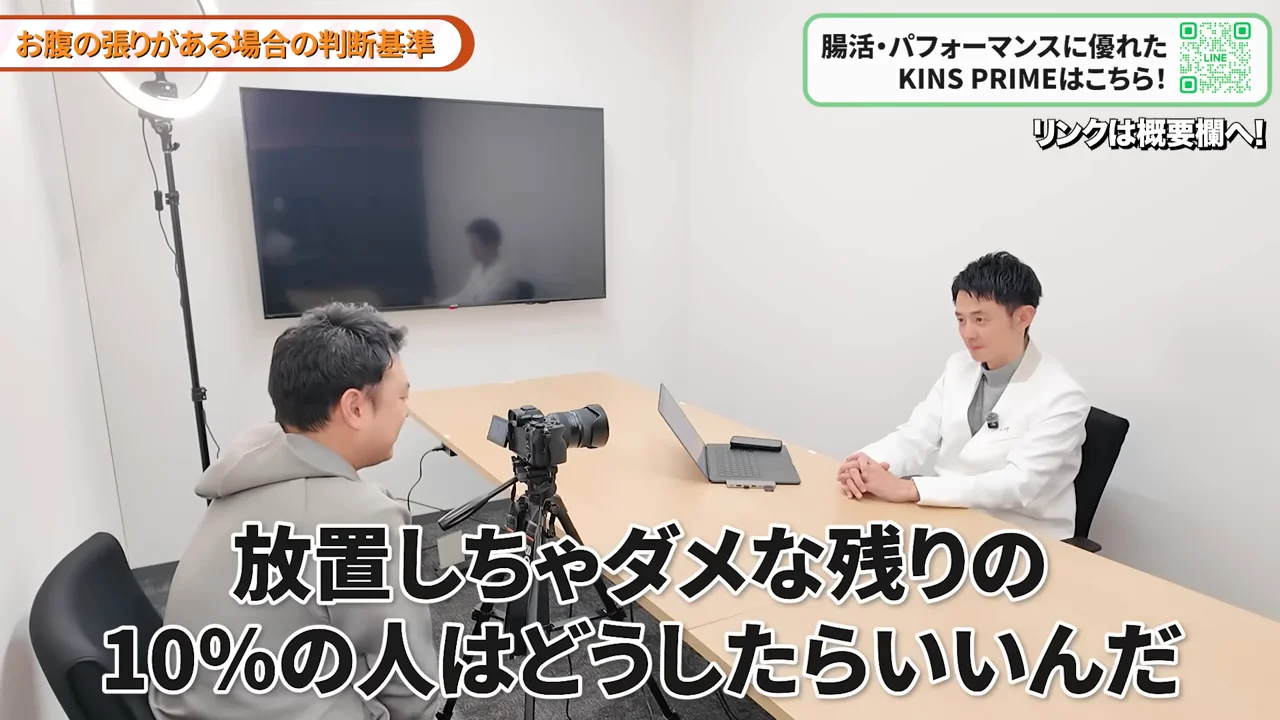 机を挟んで白衣を着た男性とパーカー姿の男性が座っています。