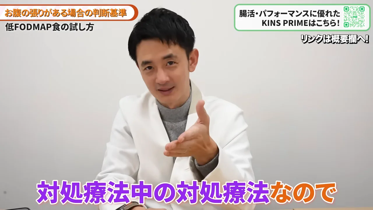 白衣を着た男性が正面に向かって手を差し出しながら話しています。