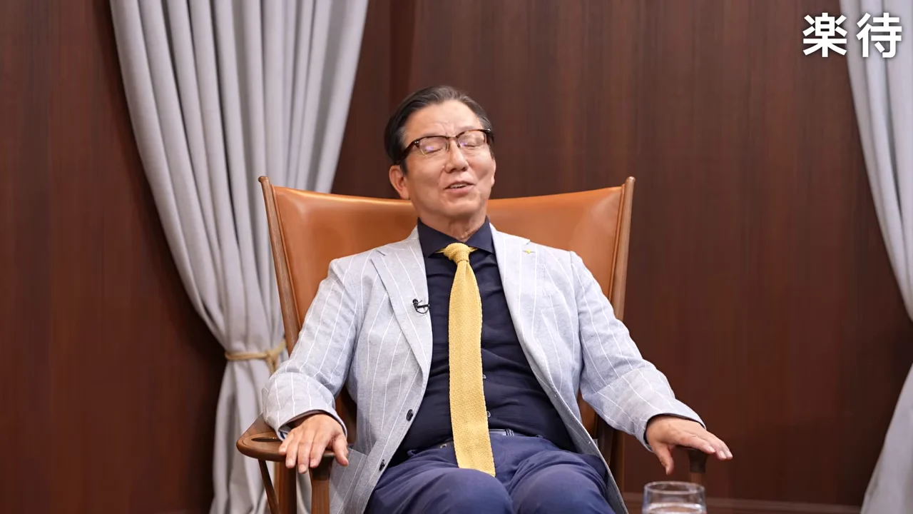 グレーのジャケットを着た男性が椅子に座って話している様子
