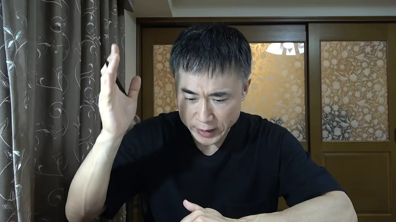 黒いTシャツを着た男性が右手を挙げながら話している。