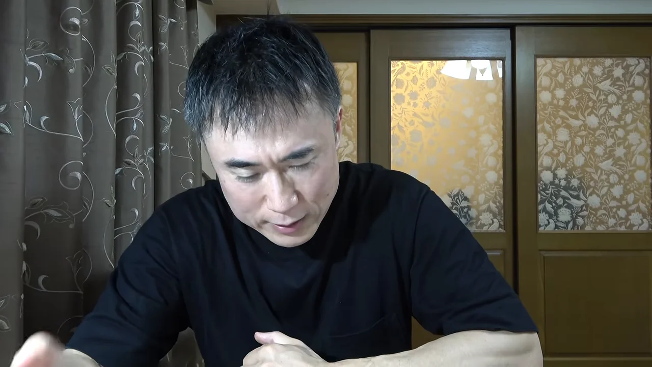 黒いTシャツを着た男性が下を向きながら話している様子。