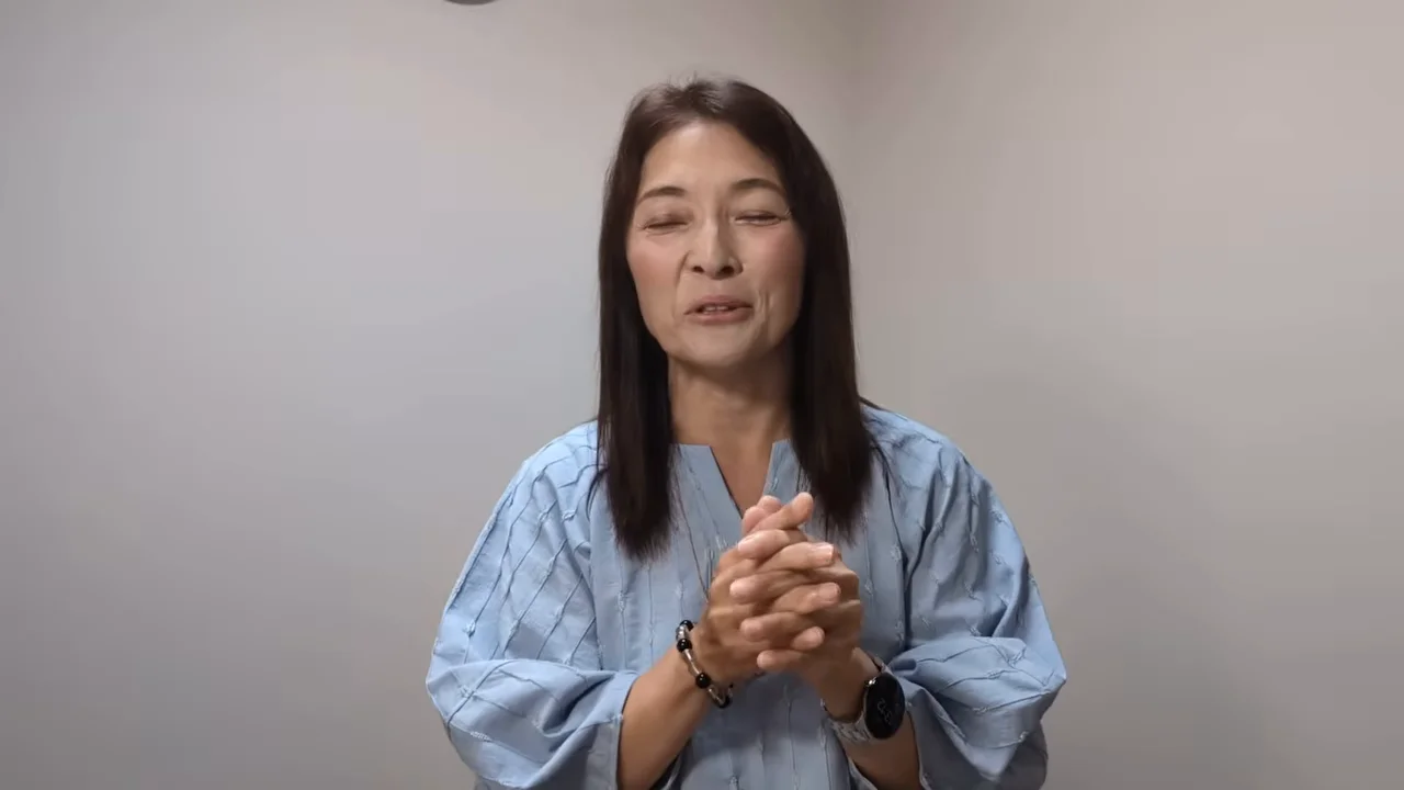 水色の服を着た女性が胸の前で手を組んで話している様子。