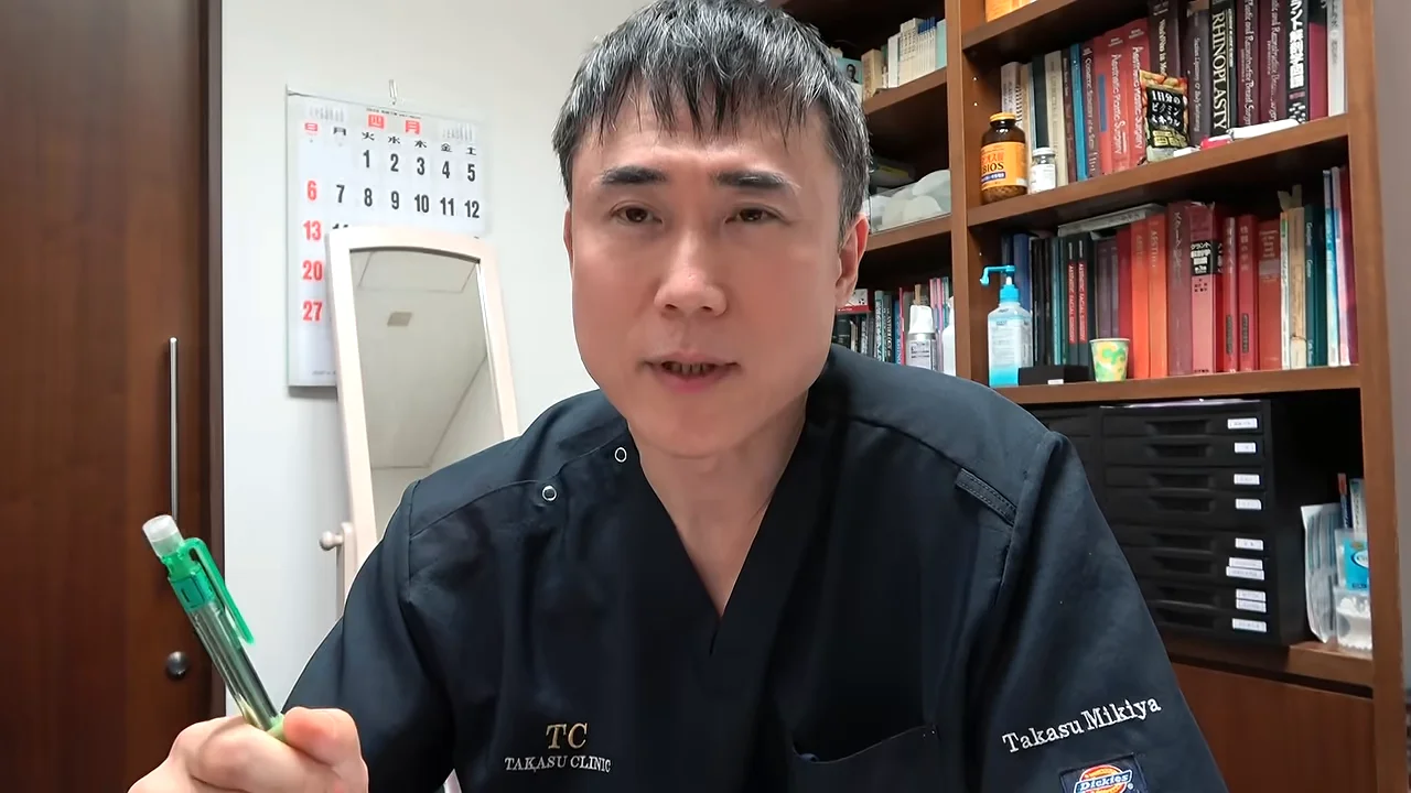 右手に緑色のペンを持ちながら正面を見つめて話す男性