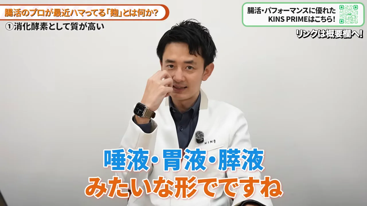 白衣を着た男性が鼻のあたりに手を添えながら話している様子。