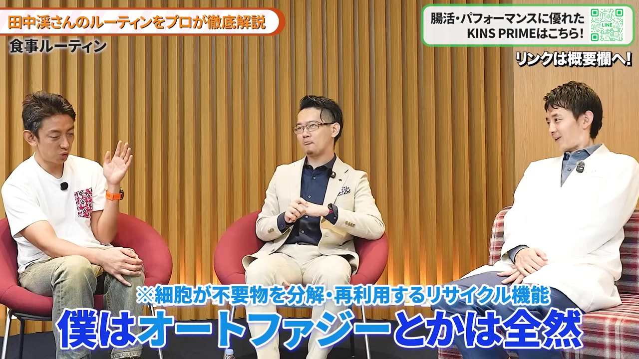並んで座る3人の男性のうち、左側の男性が手を上げて話しています。