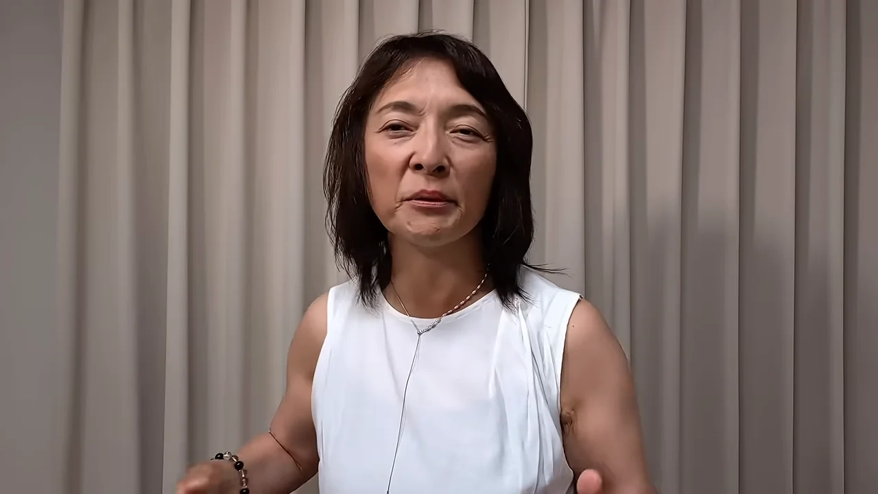 カーテンの前に立つ、白いノースリーブを着た女性。