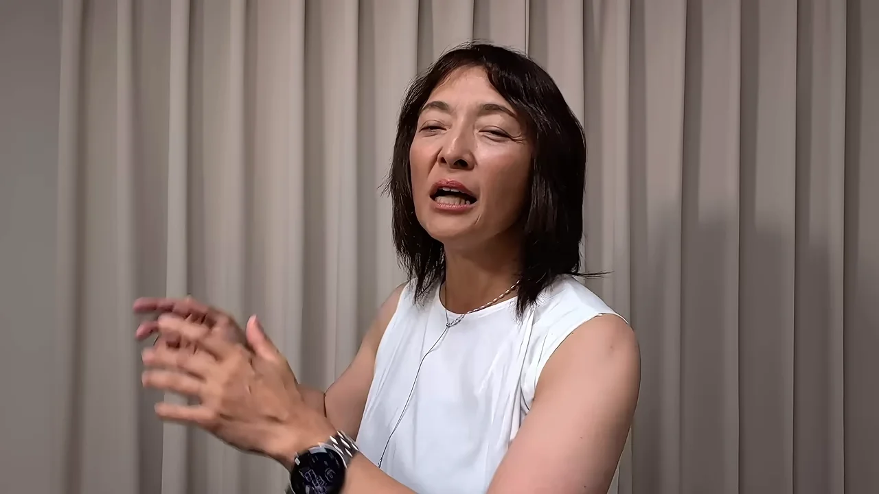 身振り手振りを交えながら話す、白いノースリーブを着た女性。