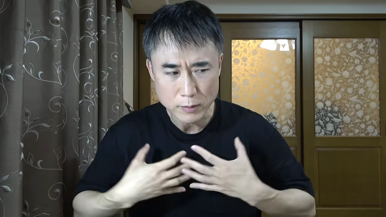 黒いTシャツを着た男性が、胸の前で両手を広げながら話しています。