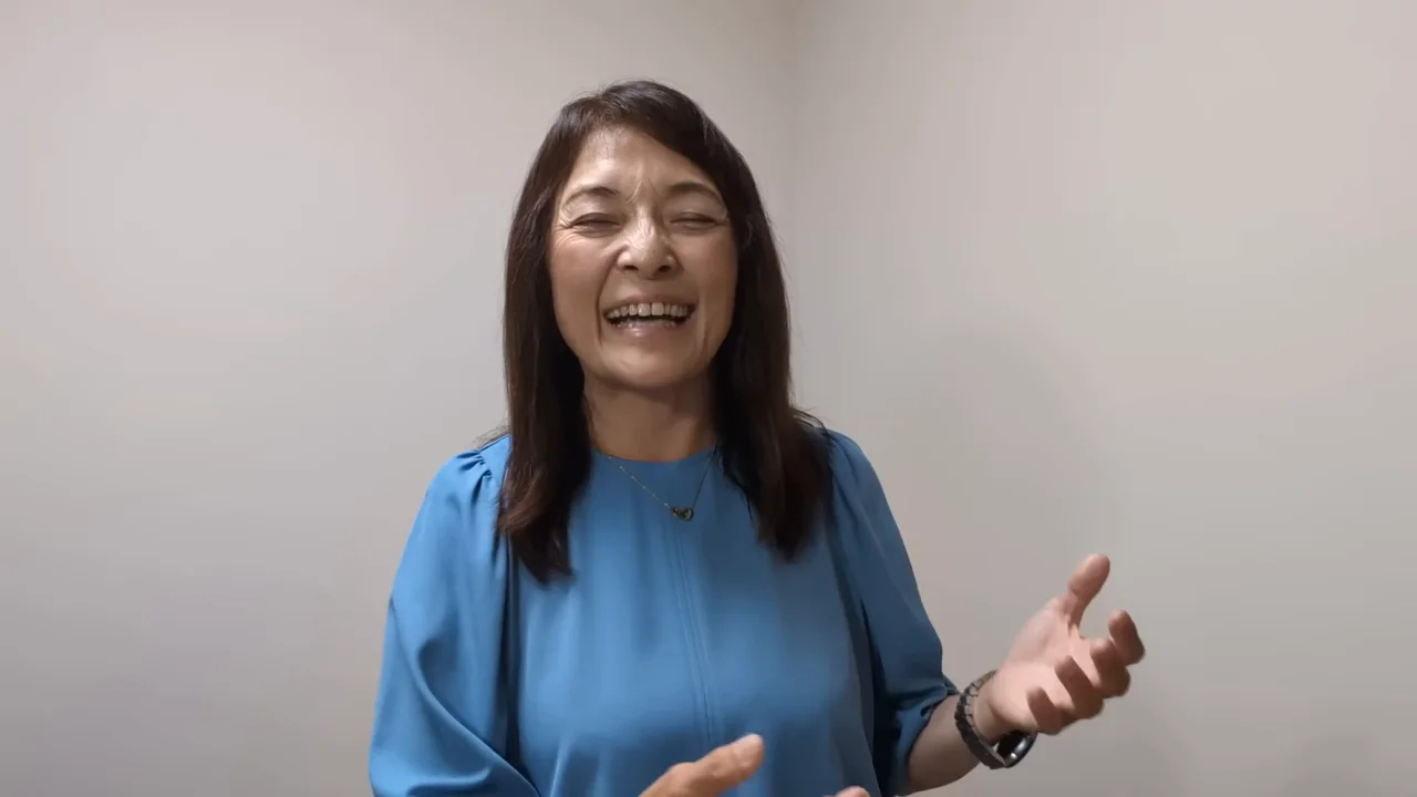 青い服を着た女性が笑顔で身振り手振りを交えながら話している様子。
