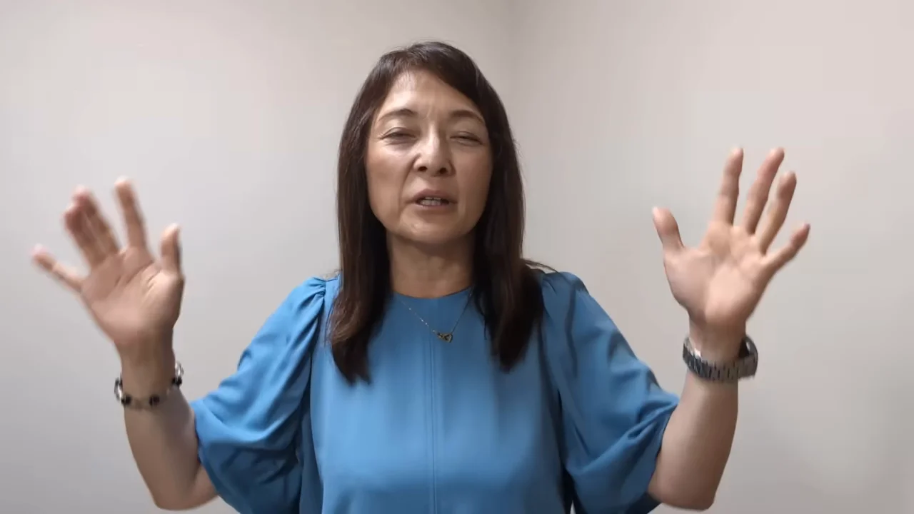 青い服を着た女性が両手を広げて掲げながら説明している様子。