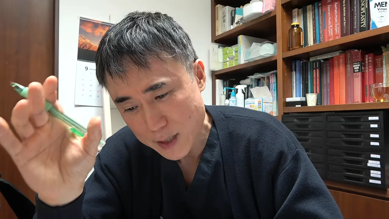 男性がペンを持った右手を掲げながら、下方に視線を向けて話している様子。