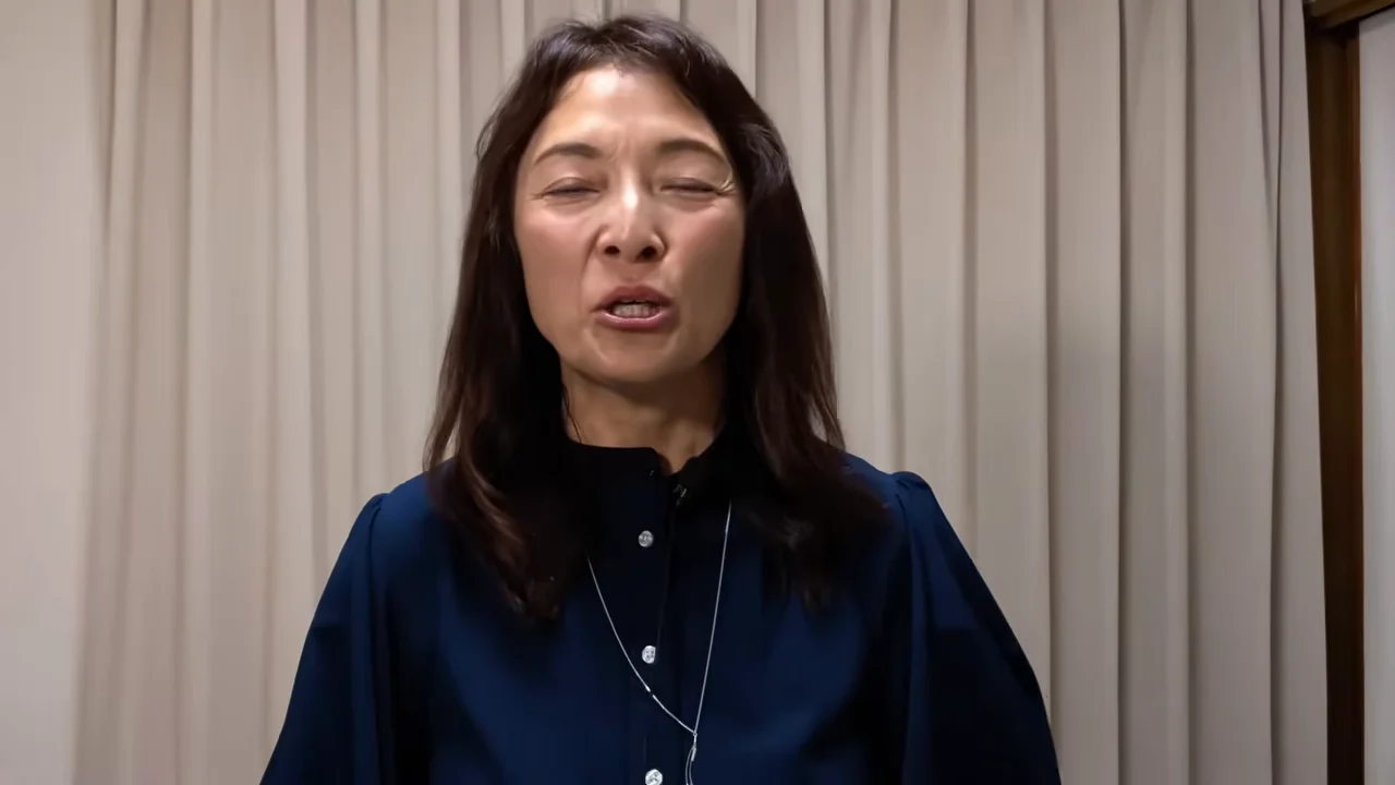 カーテンを背景に女性が正面を向いて話しています。