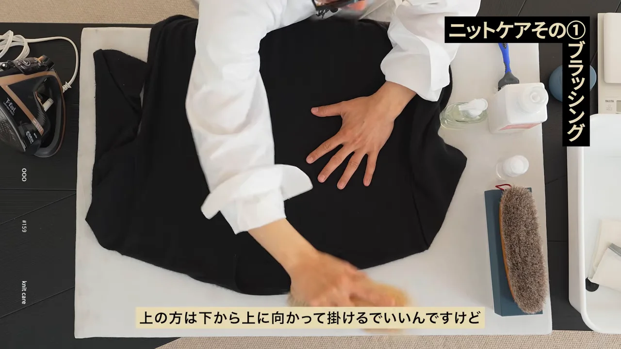 台の上に広げた黒いニットにブラシをかけている様子