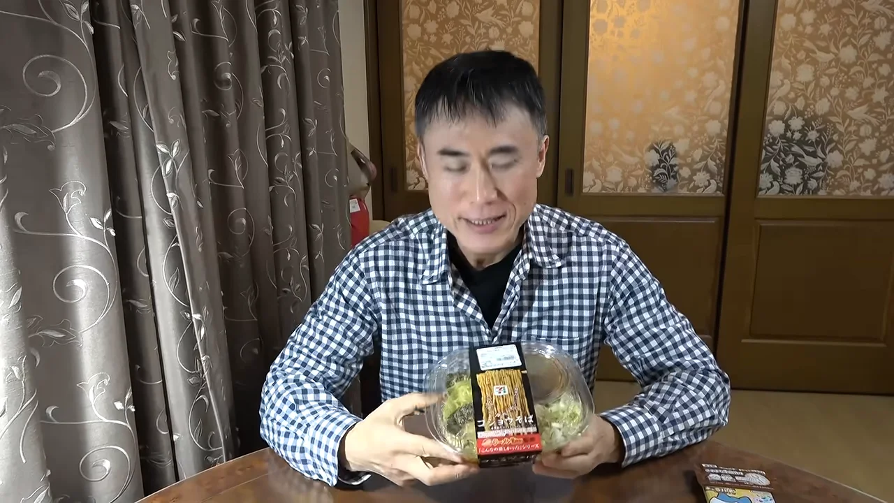 チェック柄のシャツを着た男性が、食材の入った容器をテーブルの前で両手に持っている。