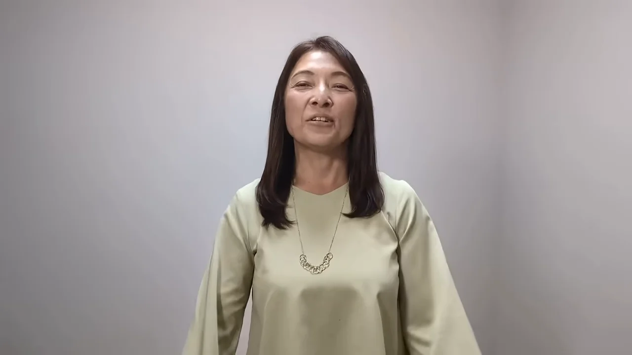 薄緑色の服を着た女性が、カメラに向かって正面を向いて話しています。