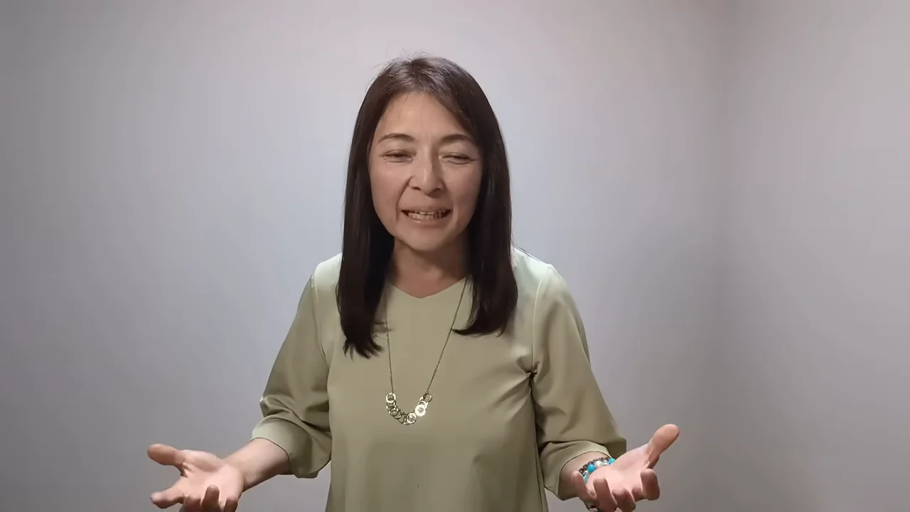 薄緑色の服を着た女性が、両手を広げるジェスチャーを交えながら話しています。
