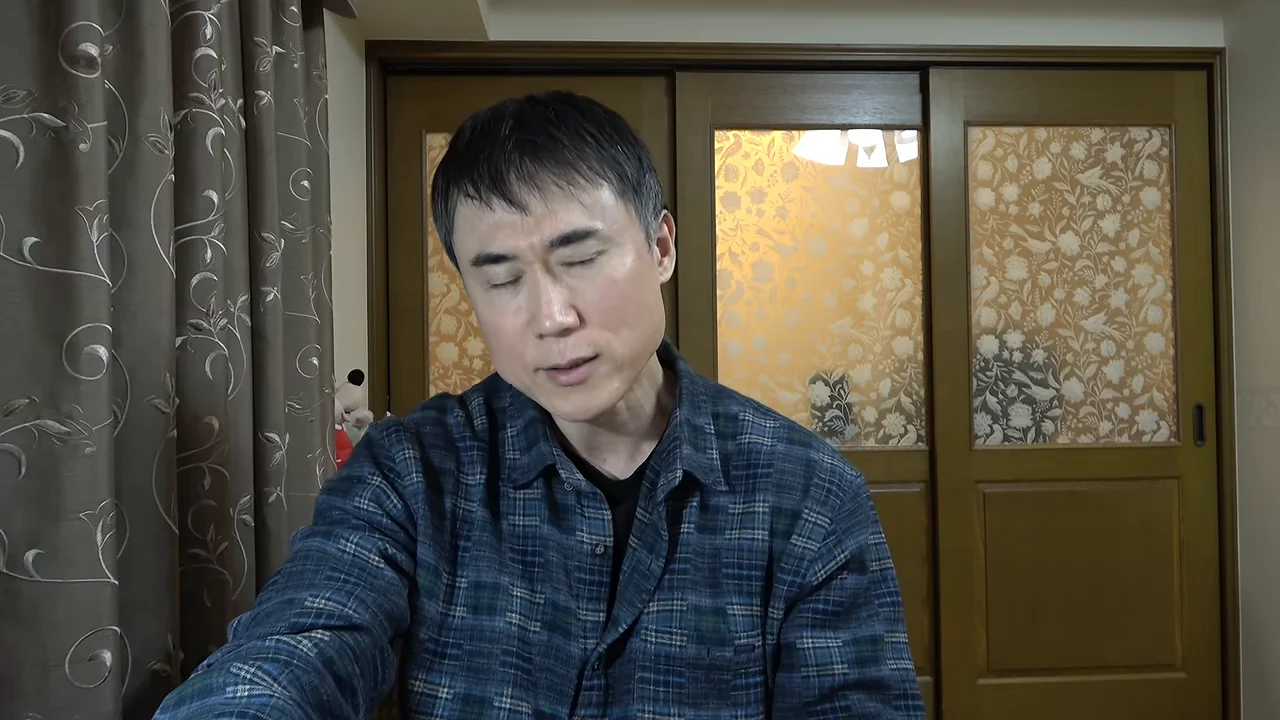 室内でチェック柄のシャツを着た男性が静かに語りかけている様子