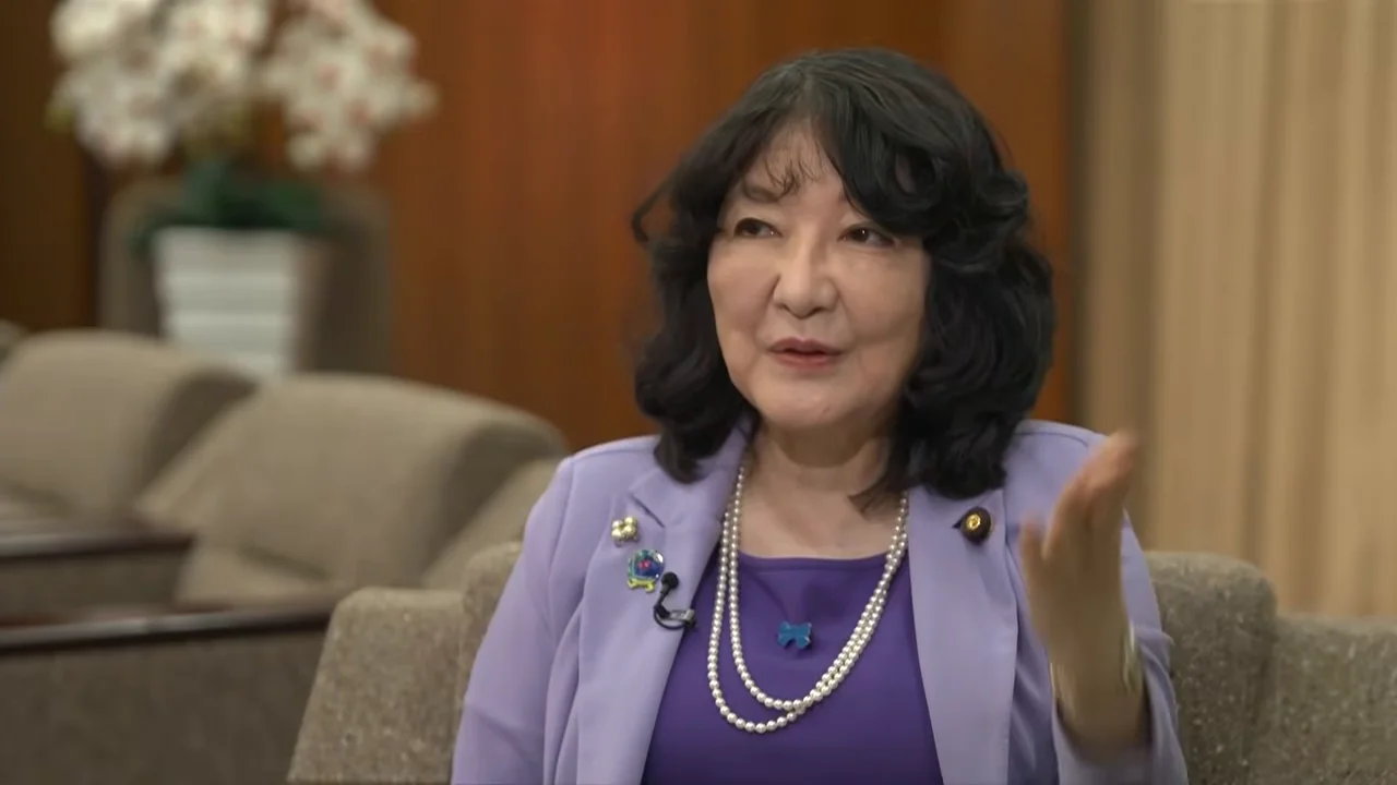 女性が左手を上げてジェスチャーを交えながら説明を続けています。