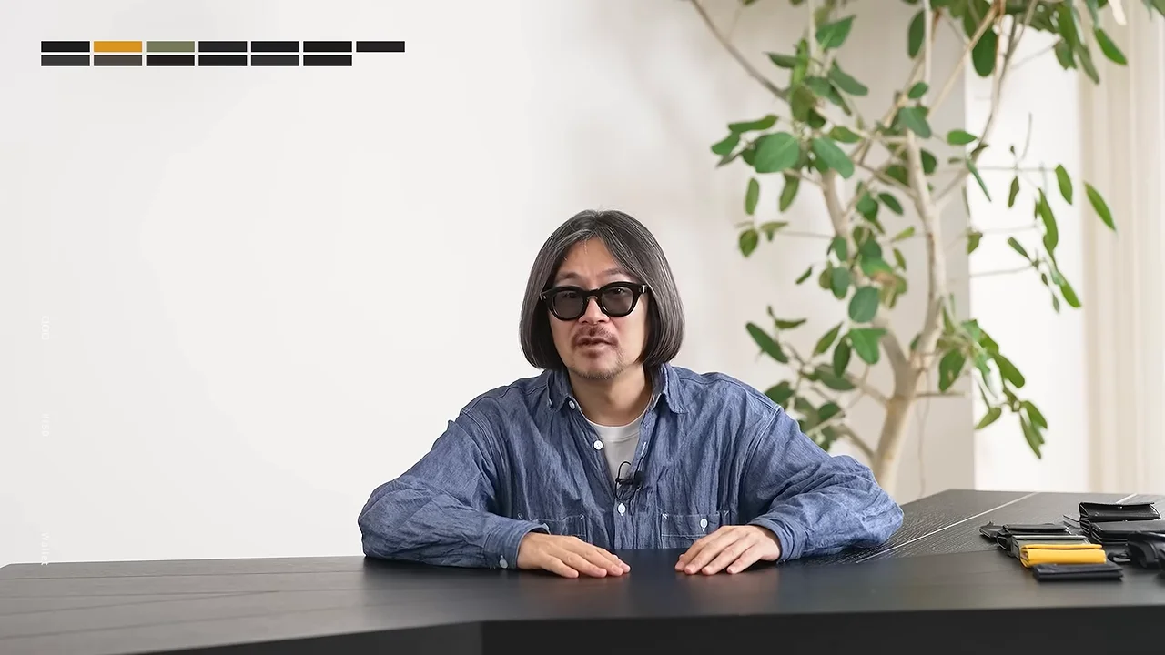 サングラスをかけた男性が机の前に座り、机の上には財布が並べられています。