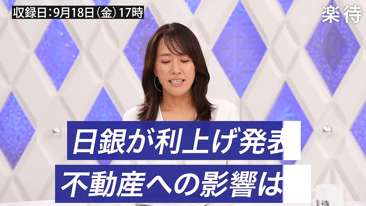 スタジオで白い服を着た女性司会者が下を向いて原稿を読んでいる様子。