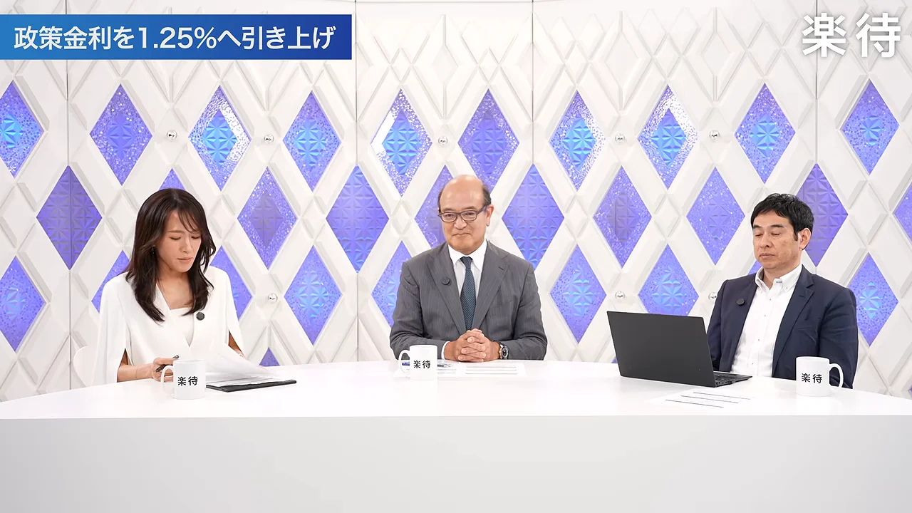 スタジオの白いテーブルに女性と男性2人の計3人が並んで座っている様子。