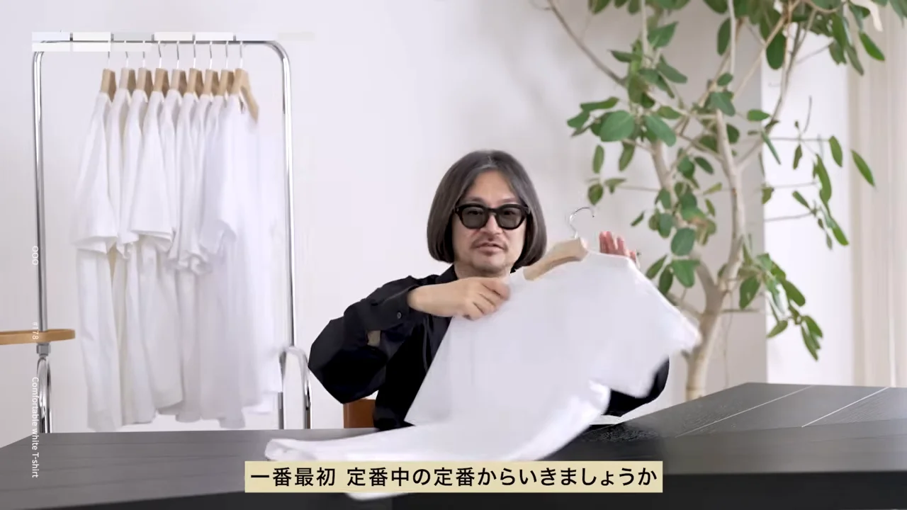 黒いシャツを着た男性が、ハンガーにかけた白いTシャツを持ち上げている様子。