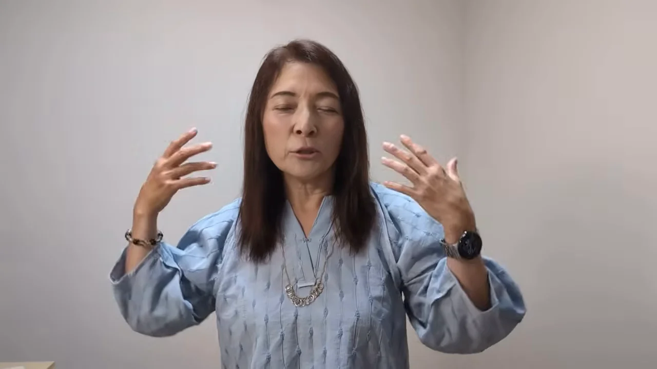 両手を顔の横に掲げながら話す女性の様子が捉えられています。