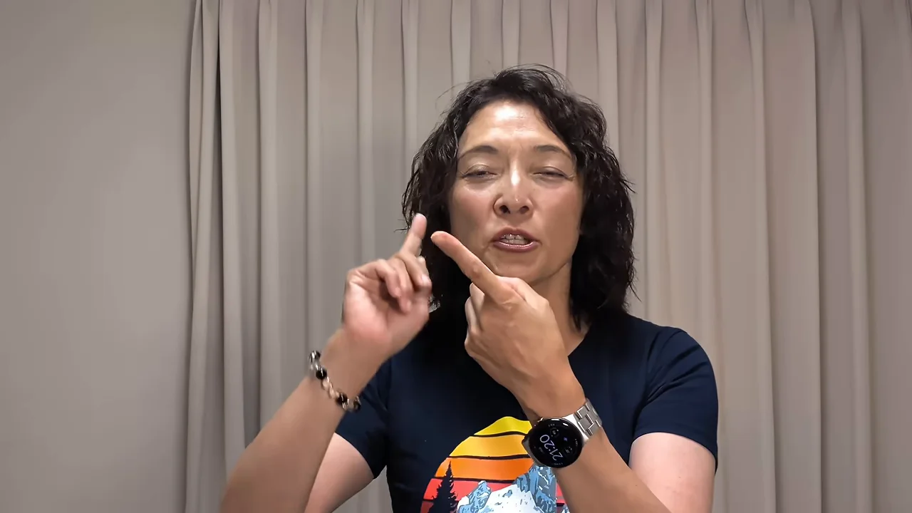 カーテンの前に立ち、両手の人差し指を立てて話す女性