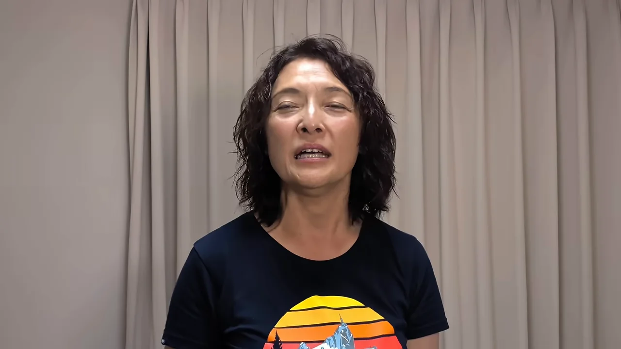 カーテンの前に立ち、カメラに向かって話す女性