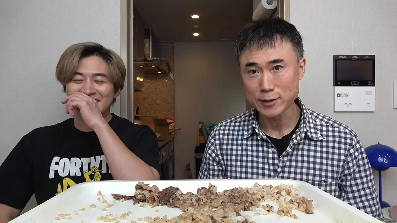 料理を前に並んで座る2人の男性のうち、右側の男性が話し、左側の男性が口元を押さえて笑っている様子。