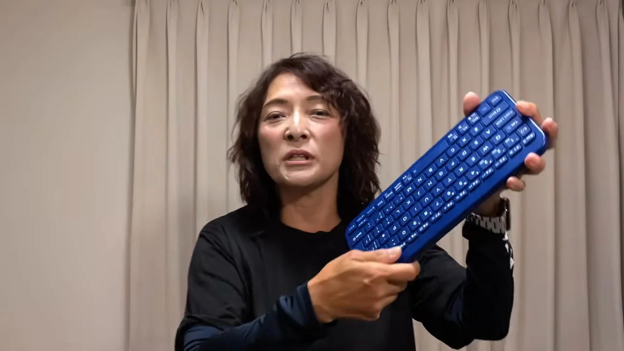 青いキーボードを両手で持ちながらカメラに向かって話す女性。