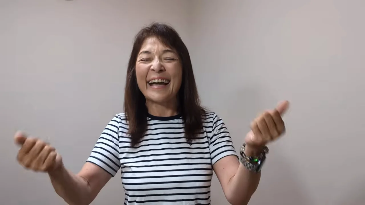 ボーダー柄の服を着た女性が笑顔で両手を挙げている様子。