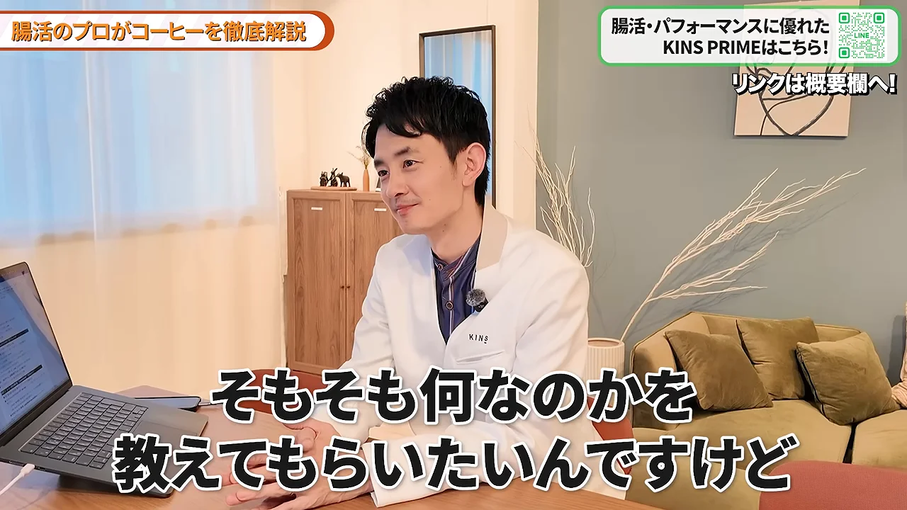 ノートパソコンが置かれたテーブルの前で話す白衣の男性