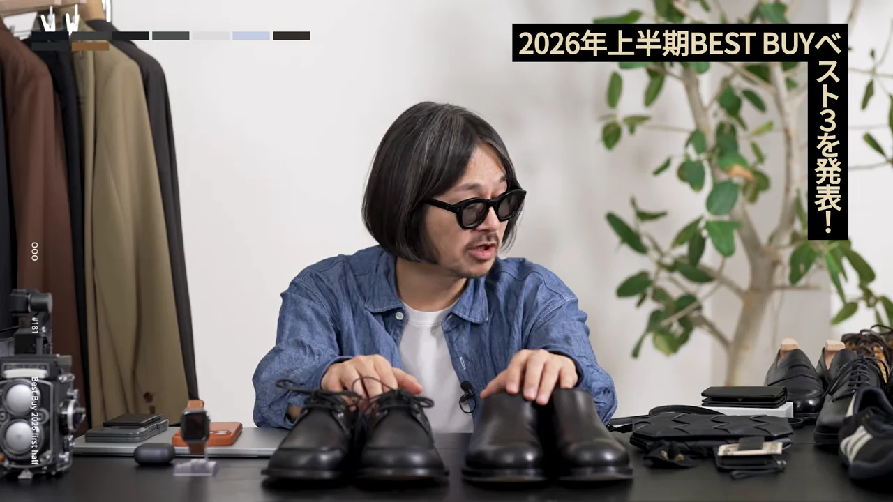 男性がテーブルに並んだ複数の黒い靴に手を添えている。