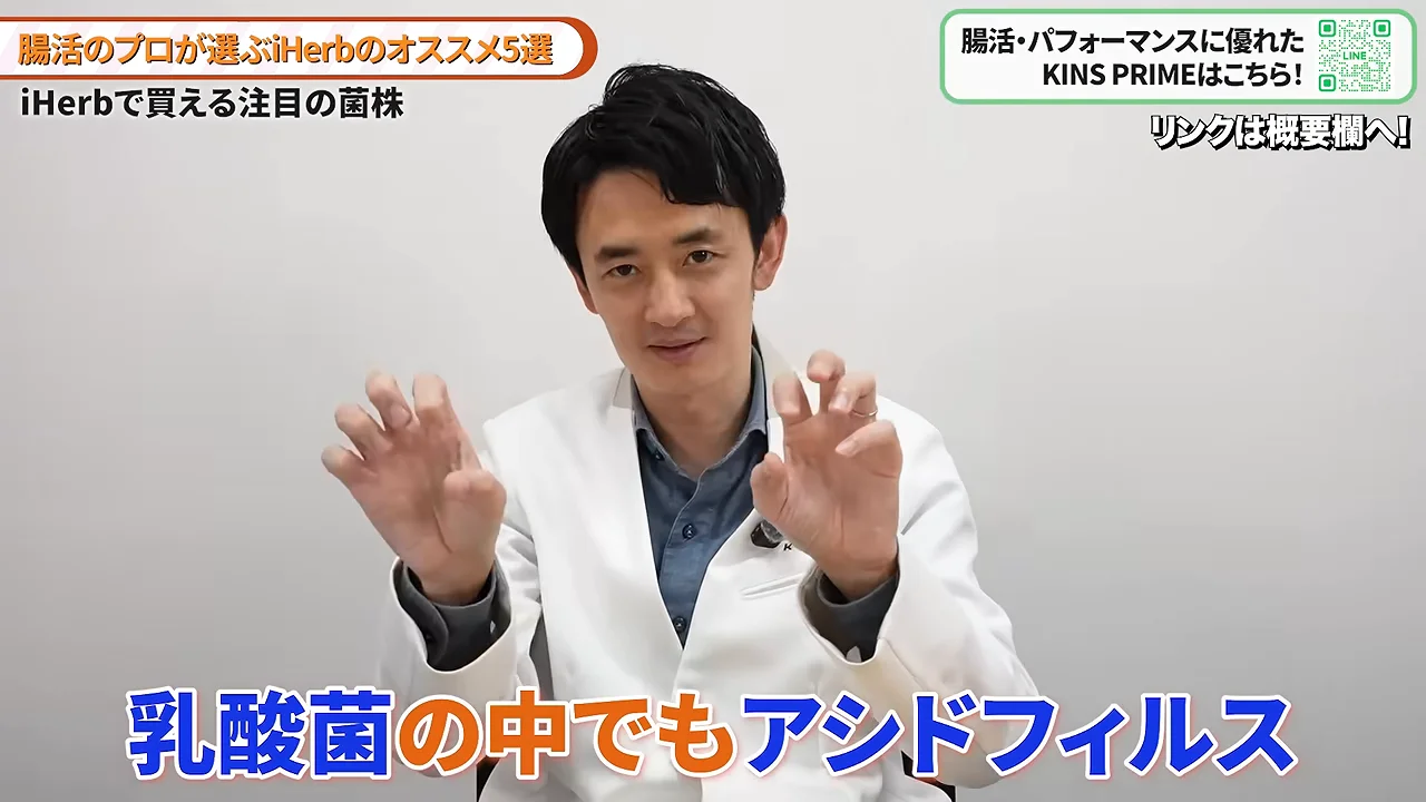 白衣を着た男性が両手を前に出しながら説明しています。