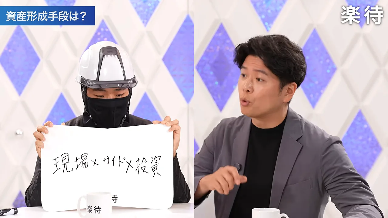 ヘルメットとマスクを着用した人物がフリップを掲げ、スーツの男性が身振り手振りを交えて話しています。